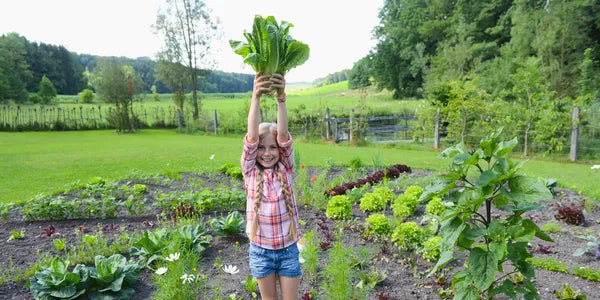 Girl holding up a bundle of greens in a garden
